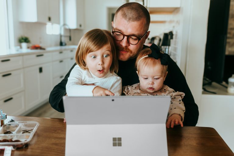 Dad holds two kids who point at wireless laptop