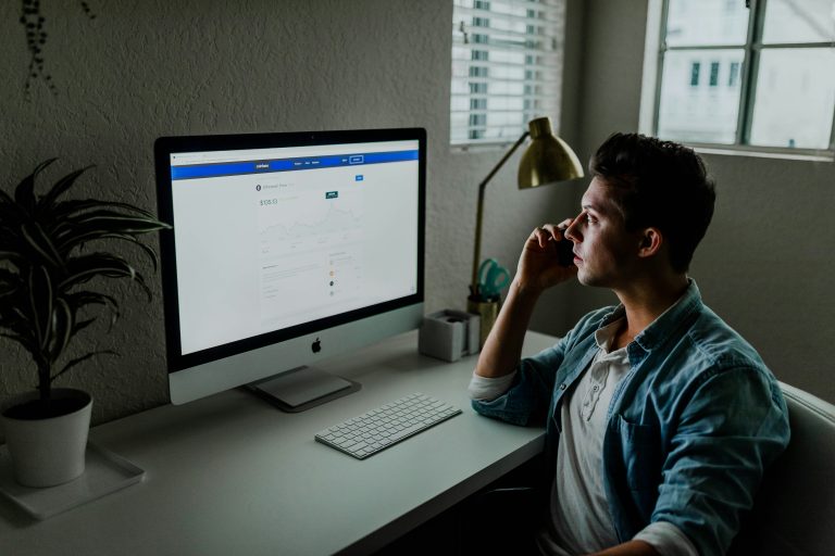 Man is on a call on the phone while looking at bright computer monitor showing data