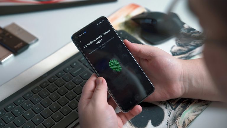 Phone with digital thumbprint scanner on screen held by person in front of keyboard and mouse