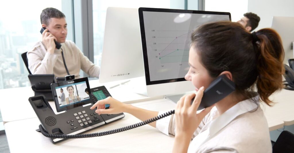 Man and woman at a shared desk using Yealink phones for calls and video calls.