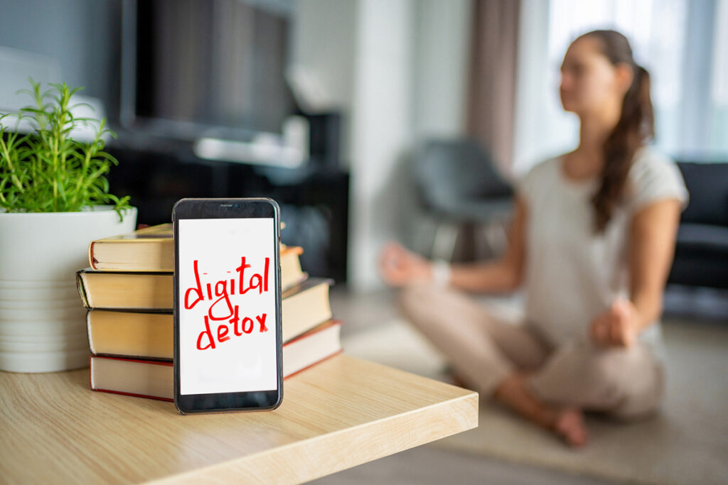 Cell phone with "digital detox" on the screen with a women doing yoga in the background.