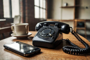 An old rotary phone and a smartphone on a wood table with a cup of coffee.