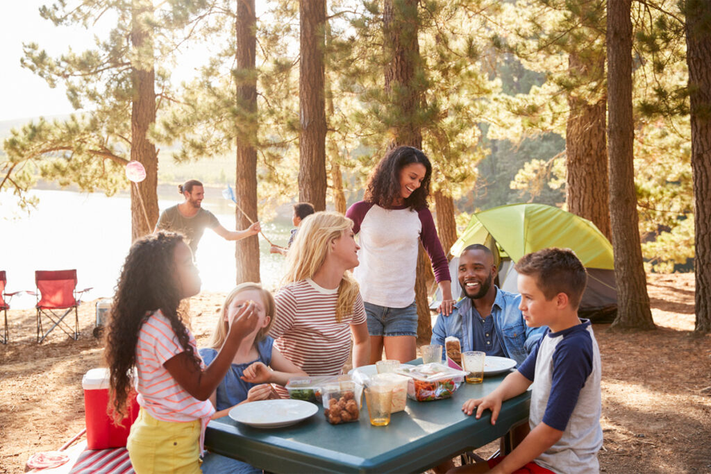Family With Friends camping by a lake surrounded by trees.