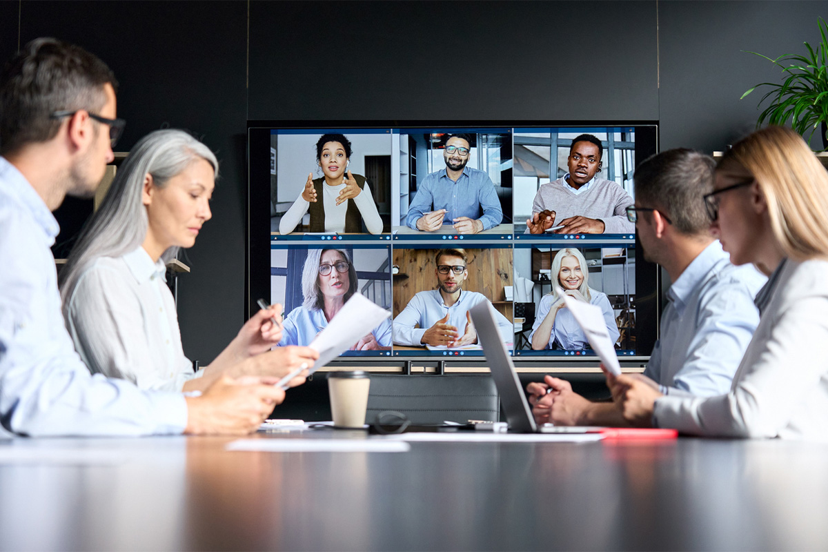 Video conference with colleagues on a screen and in person.