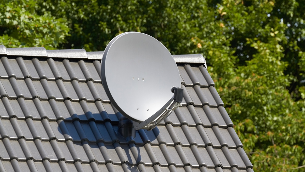 Satellite dish on a peaked roof with trees in the background.