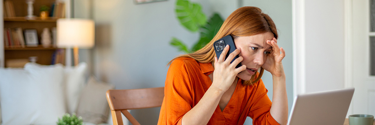 Worried businesswoman sitting at home talking on the phone and looking at laptop.