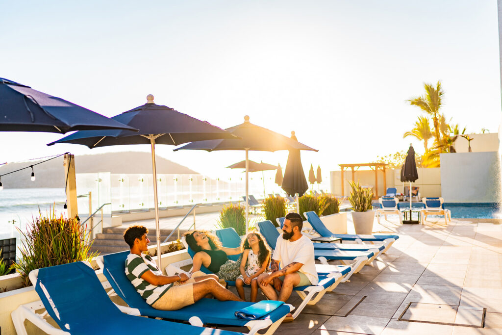 Family laughing by the pool on lounge chairs.