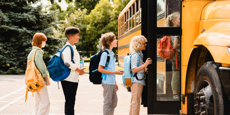 Multi-ethnic students lining up for the yellow school bus.
