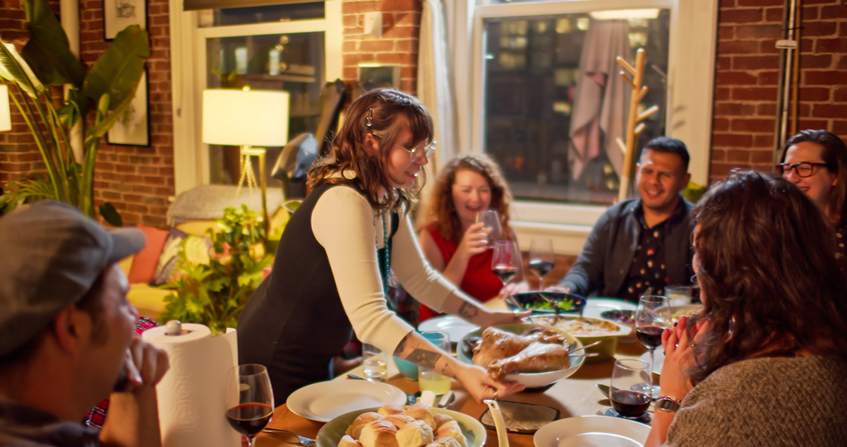 A woman bringing a platter of roast turkey to a group of people