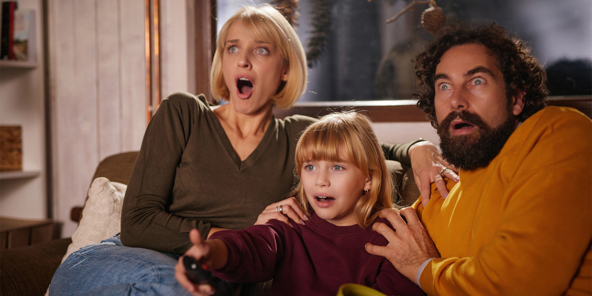 Family including a child and two adults reacting with fear while watching a scary movie