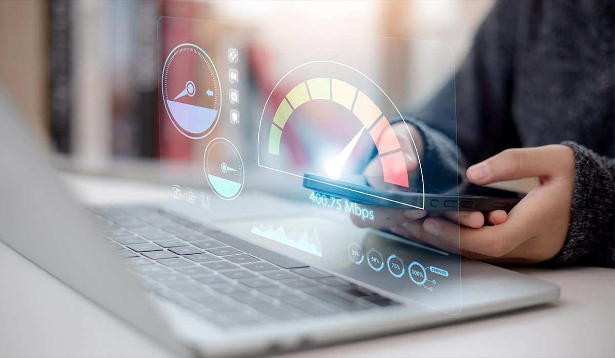 Person's hand holding smartphone with open laptop. Virtual screen of Internet speed measurement.
