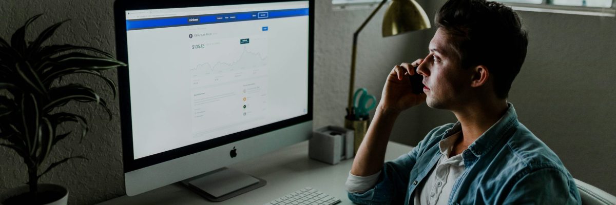 Man is on a call on the phone while looking at bright computer monitor showing data