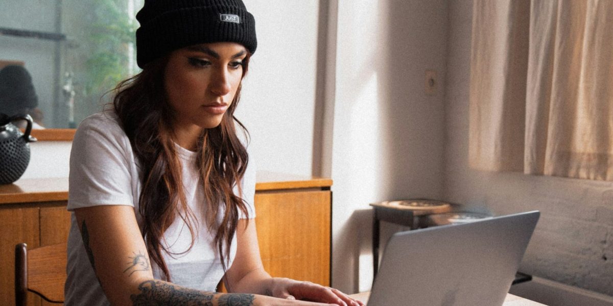 Female photographer looks at laptop while typing looking concentrated, camera lying on table