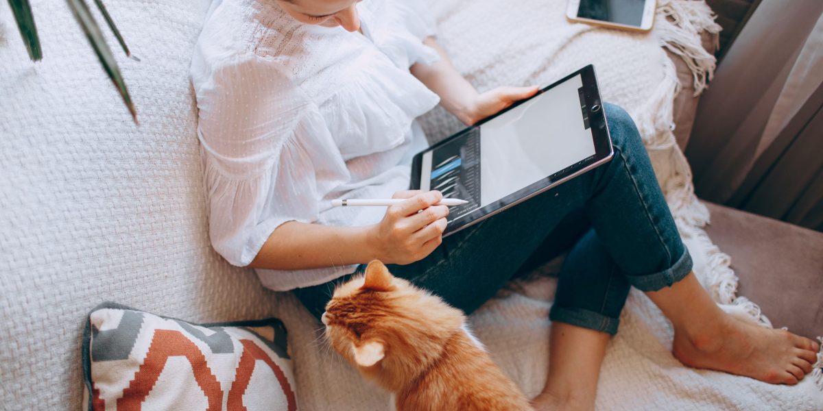 Woman sits on couch with cat drawing on wireless tablet