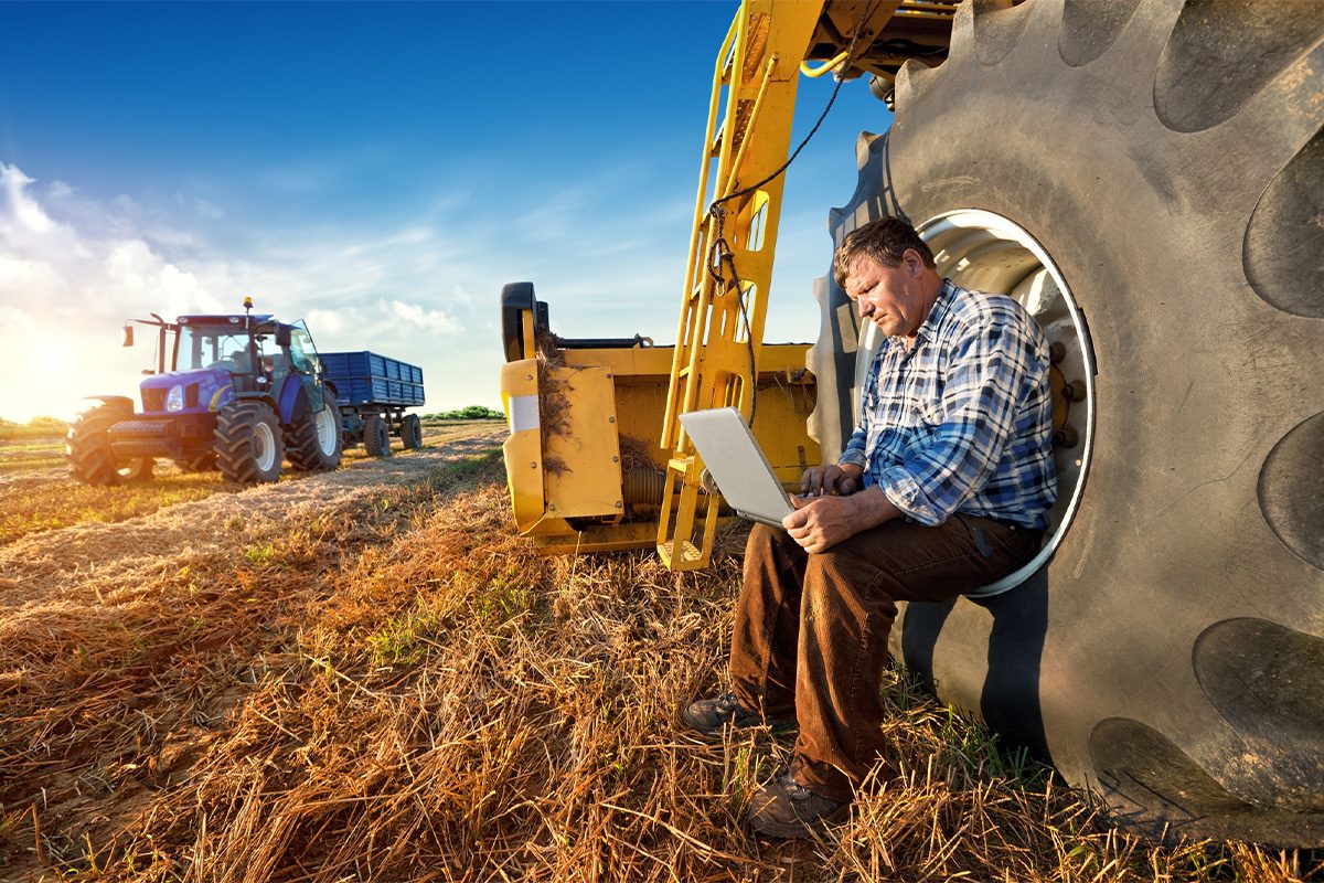 Farmer on a laptop with farm equipment.