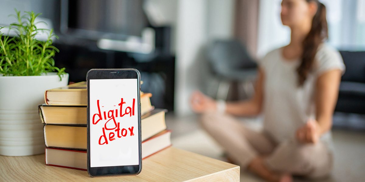 Cell phone with "digital detox" on the screen with a women doing yoga in the background.