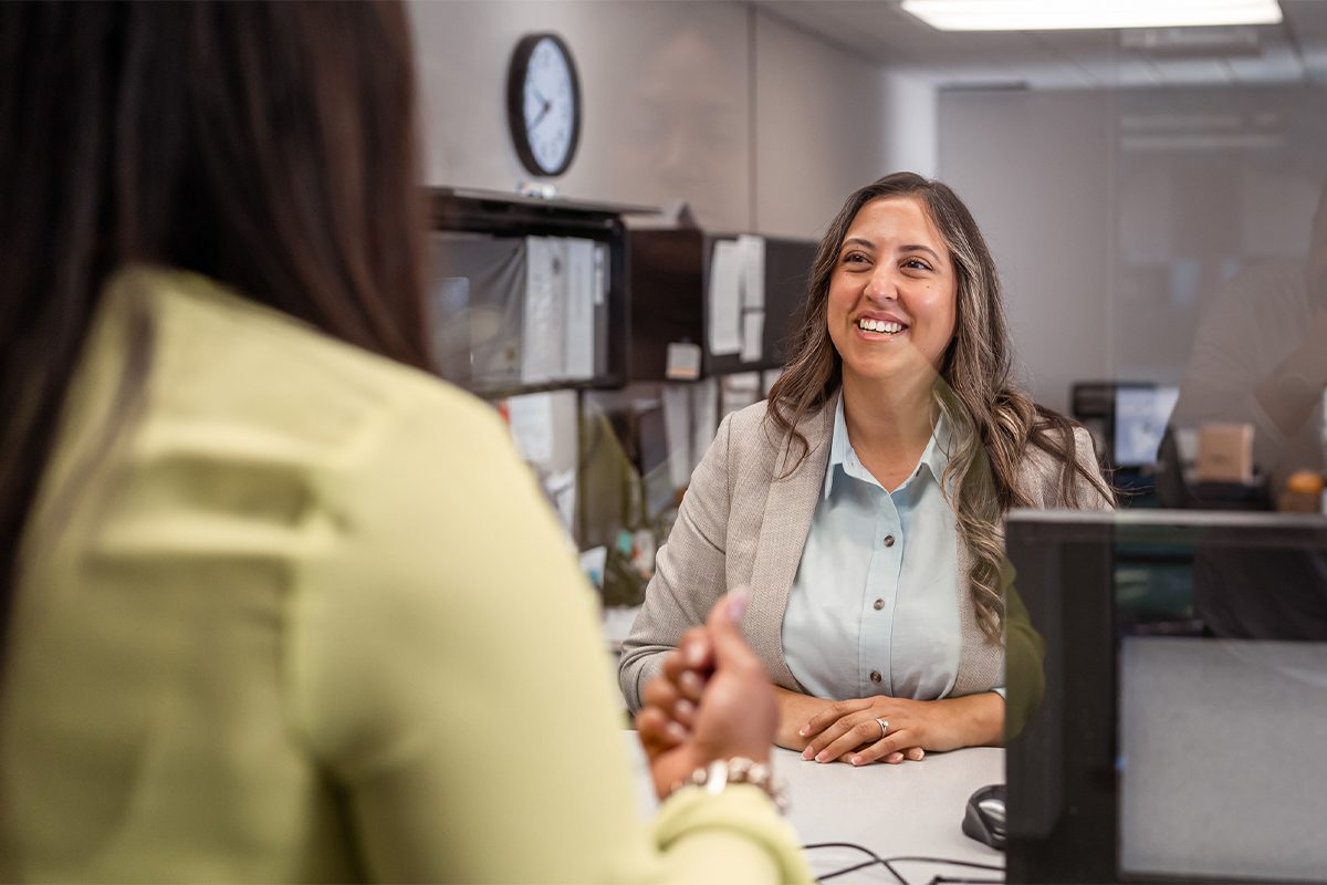 Female customer service representative greets a customer with a big smile at the counter in a bank.