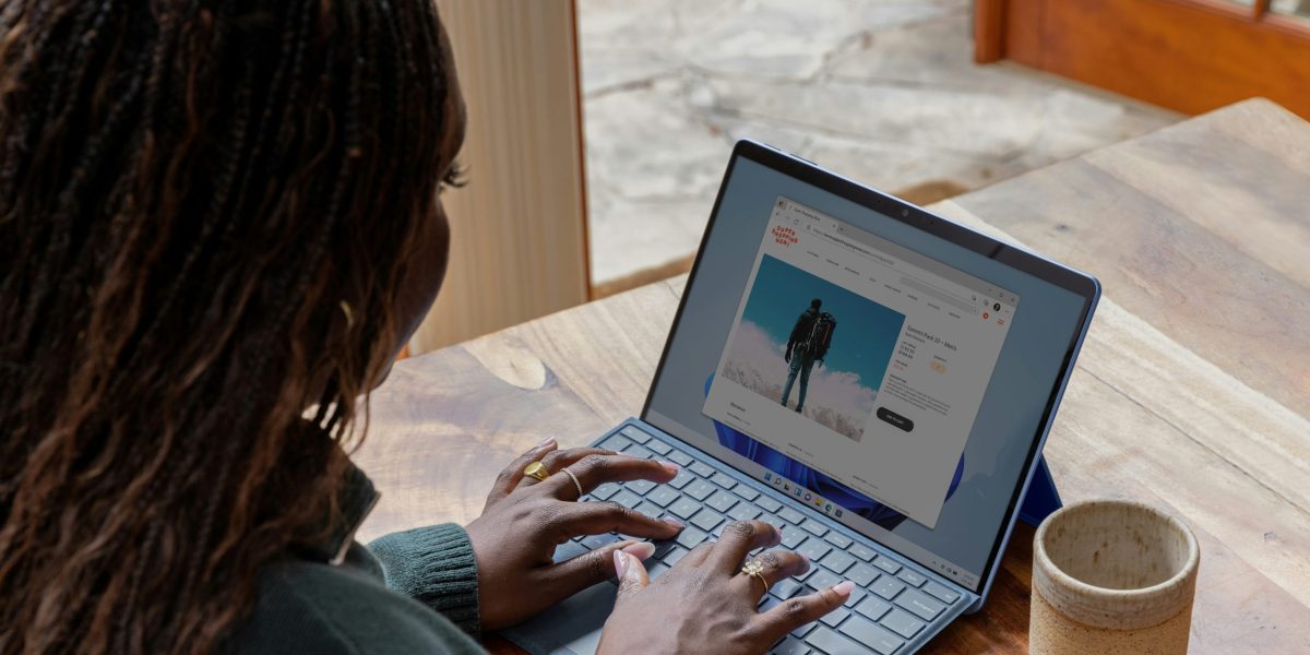 Woman with braided hair sits at a table with coffee mug while typing on a laptop showing a web search