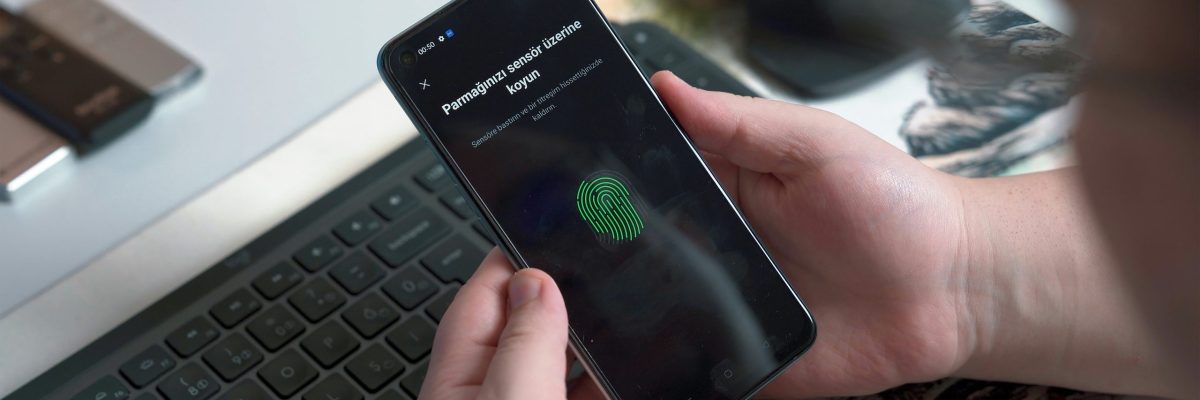 Phone with digital thumbprint scanner on screen held by person in front of keyboard and mouse