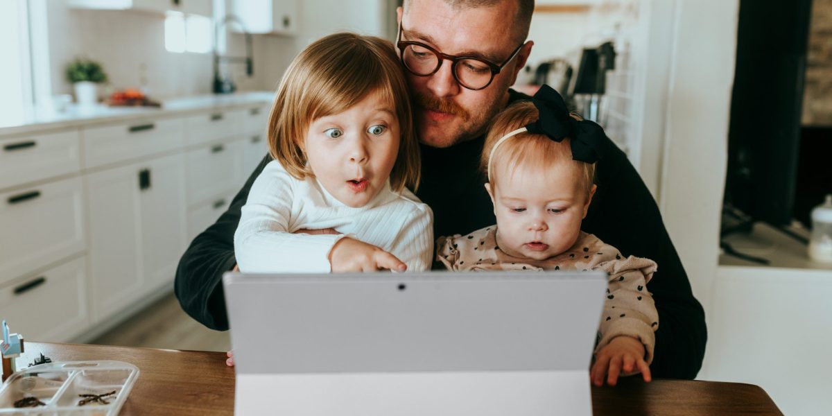 Dad holds two kids who point at wireless laptop