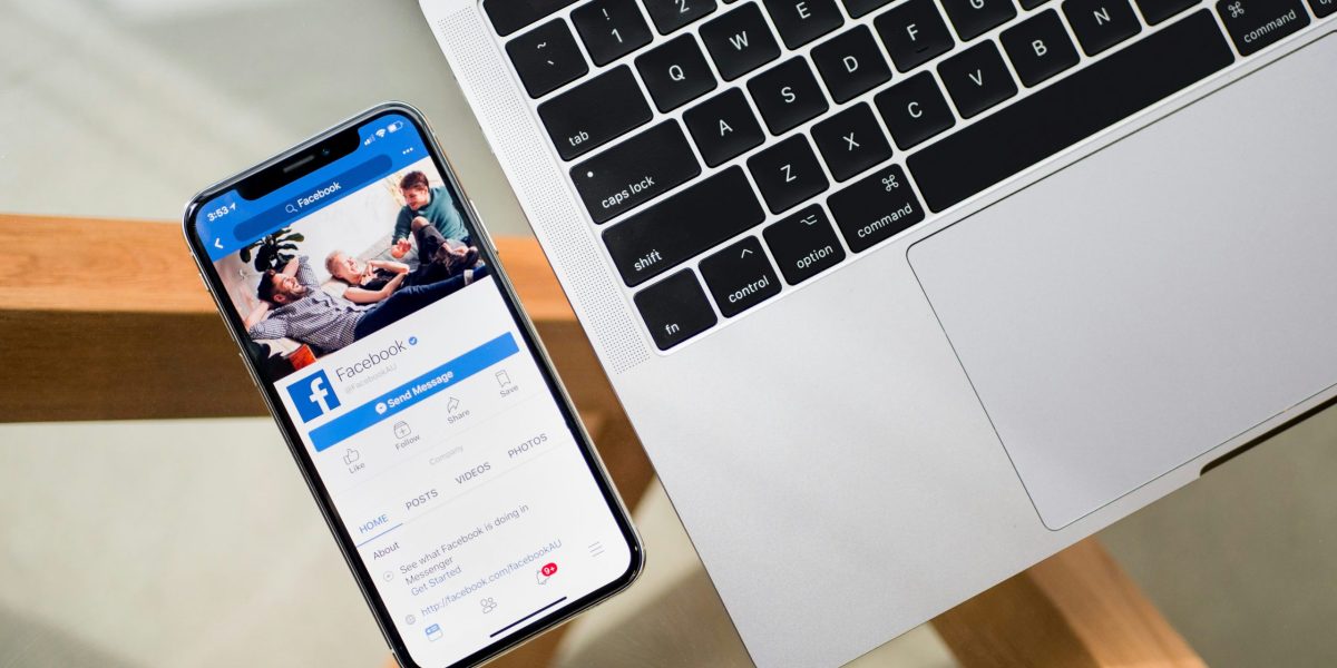 Phone lies next to laptop showing a Facebook page